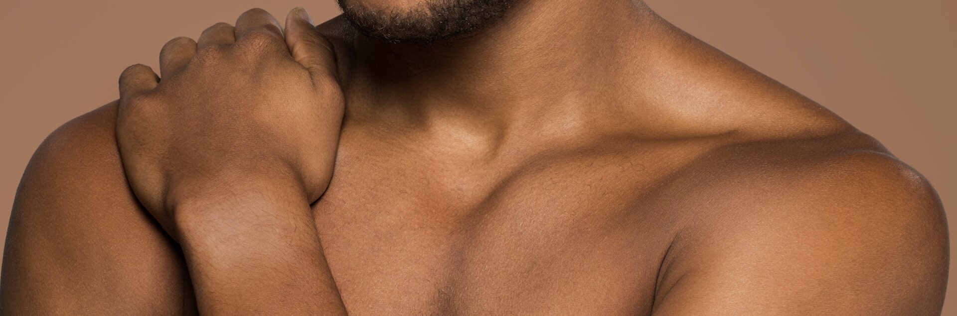 Een vrouw, gezien op haar rug, die haar schouder wast met een rijk schuim. Haar hand rust op de ingezeepte huid en de achtergrond is effen beige.