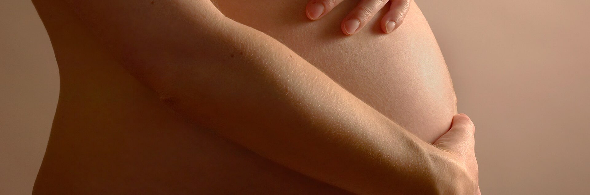 Een vrouw, gezien op haar rug, die haar schouder wast met een rijk schuim. Haar hand rust op de ingezeepte huid en de achtergrond is effen beige.