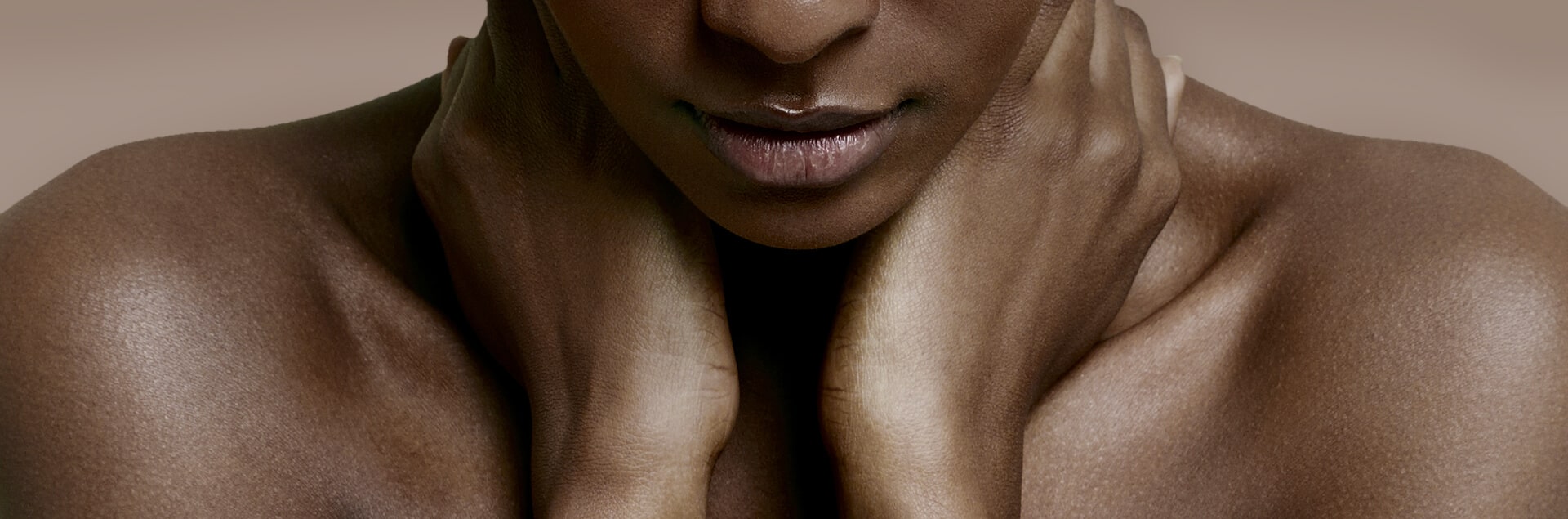 Een vrouw, gezien op haar rug, die haar schouder wast met een rijk schuim. Haar hand rust op de ingezeepte huid en de achtergrond is effen beige.