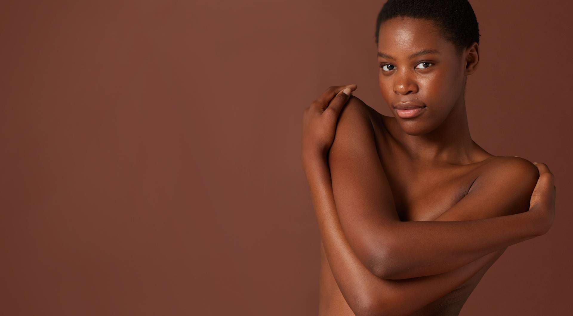 Een vrouw met een lichte huidskleur, gezien vanaf haar rug, die haar schouder inzeept met een rijk schuim tegen een beige achtergrond.